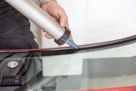 tech applying glue sealing to windshield in a garage